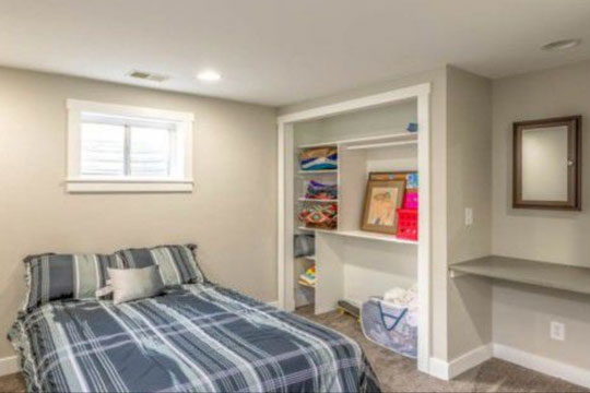 A bedroom with striped blue sheets, a cabinet, and a desk